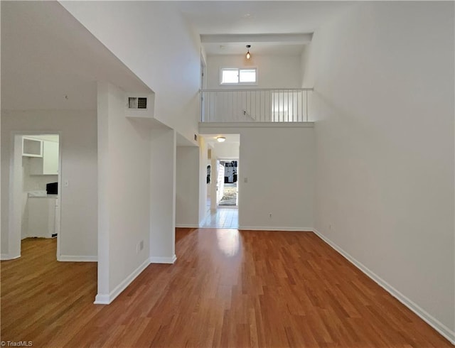 unfurnished living room featuring baseboards, a high ceiling, visible vents, and wood finished floors