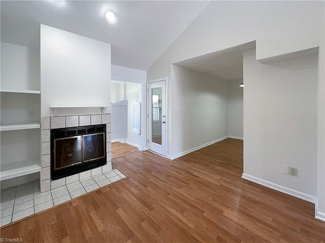 unfurnished living room featuring built in shelves, a fireplace, vaulted ceiling, wood finished floors, and baseboards