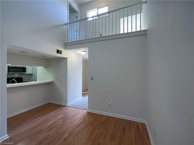 unfurnished living room featuring a high ceiling, wood finished floors, visible vents, and baseboards