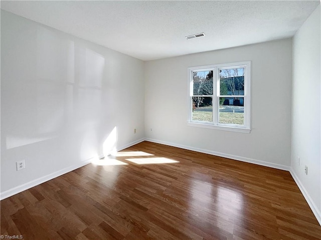 spare room with visible vents, a textured ceiling, baseboards, and wood finished floors