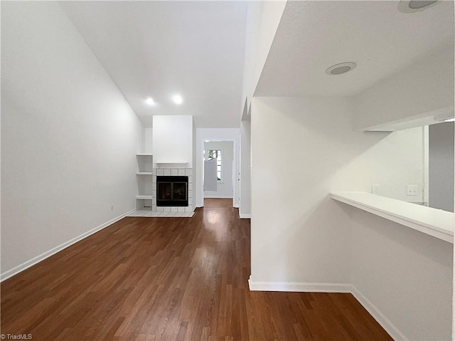 unfurnished living room featuring a tiled fireplace, baseboards, and wood finished floors