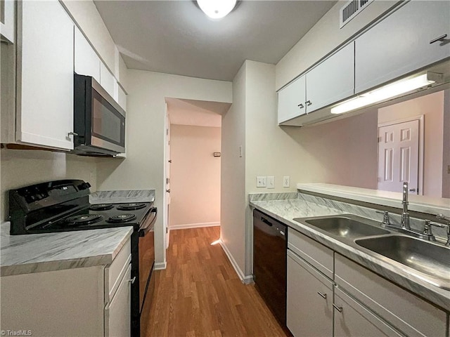 kitchen featuring black appliances, white cabinets, a sink, and wood finished floors