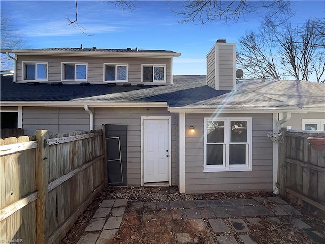 rear view of property featuring a chimney, fence, and roof with shingles