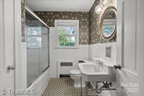 720 Ferndale Blvd, High Point, NC 27262 - bathroom with radiator heating unit, toilet, a wainscoted wall, a sink, and bath / shower combo with glass door