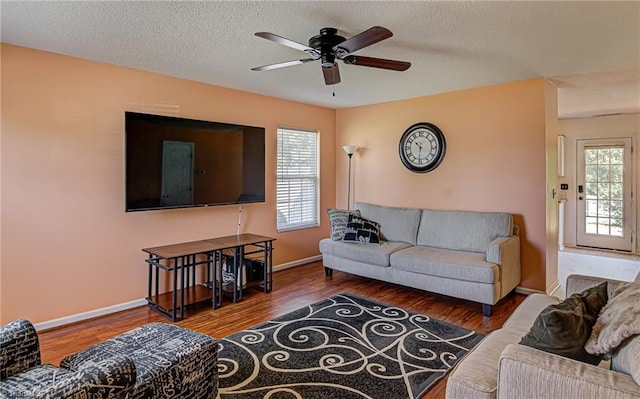 living room with a ceiling fan, wood finished floors, baseboards, and a textured ceiling