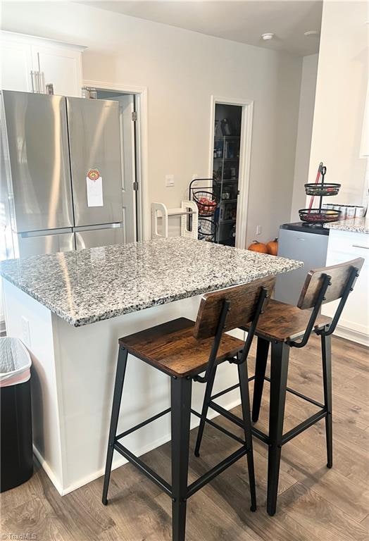 kitchen with white cabinets, a kitchen breakfast bar, light hardwood / wood-style flooring, stainless steel fridge, and light stone countertops