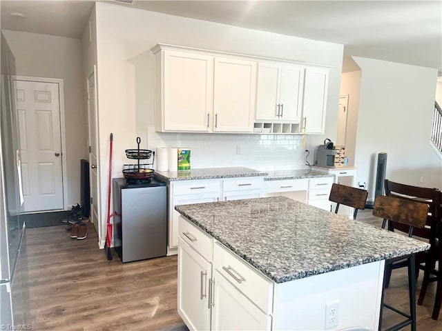 kitchen featuring white cabinetry, stone counters, decorative backsplash, a kitchen island, and hardwood / wood-style flooring