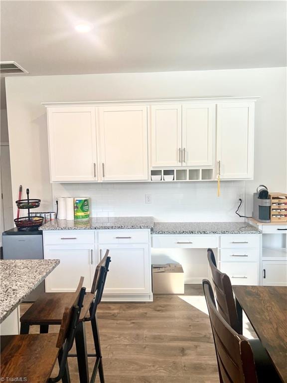 kitchen featuring hardwood / wood-style floors, decorative backsplash, light stone counters, and white cabinetry