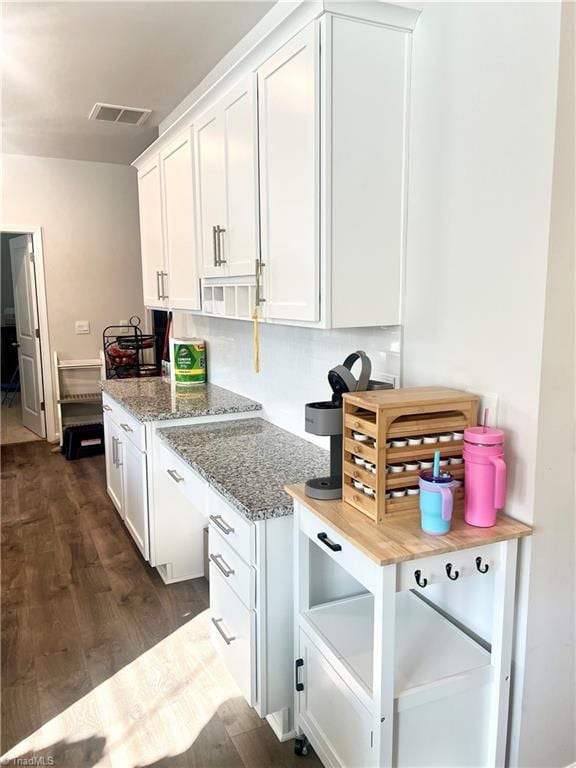 kitchen with white cabinets, backsplash, light stone countertops, and dark wood-type flooring