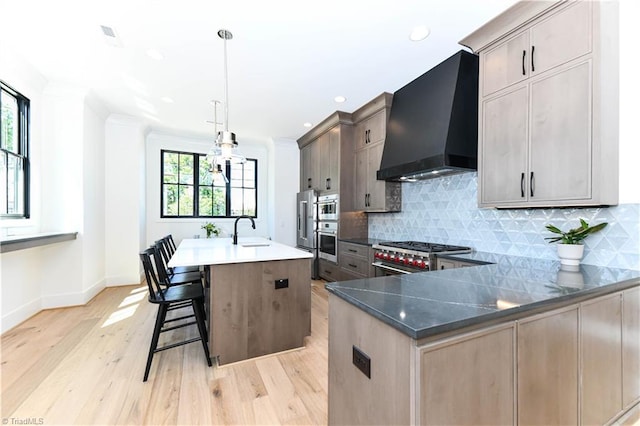 kitchen with premium range hood, a sink, backsplash, baseboards, and light wood-style floors