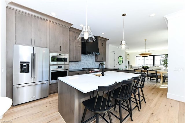 kitchen featuring light wood-style floors, appliances with stainless steel finishes, a kitchen bar, and backsplash