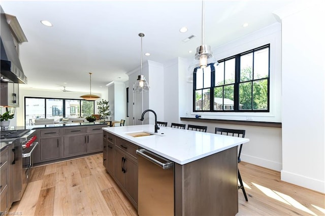 kitchen with a kitchen bar, an island with sink, a sink, stainless steel appliances, and light wood-style floors