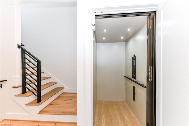 staircase featuring recessed lighting, elevator, and wood finished floors