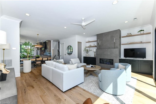 living area featuring a fireplace, crown molding, light wood-style flooring, and a ceiling fan