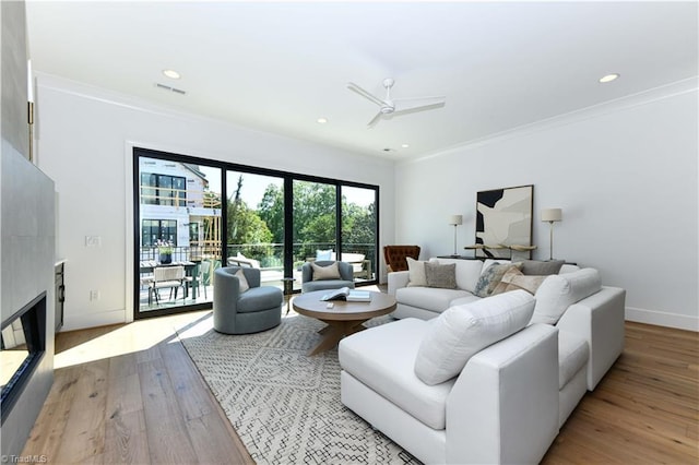 living room with crown molding, light wood-type flooring, visible vents, and a ceiling fan