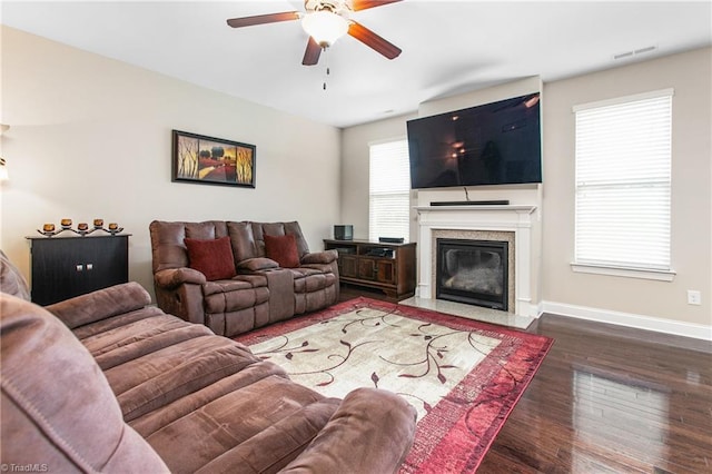 living area featuring a premium fireplace, baseboards, visible vents, ceiling fan, and wood finished floors