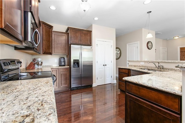 kitchen with pendant lighting, light stone counters, a sink, stainless steel appliances, and dark wood-style floors