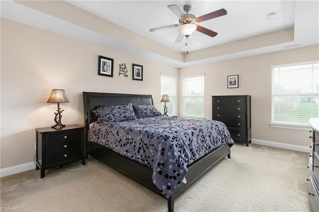 bedroom featuring light colored carpet, a raised ceiling, baseboards, and a ceiling fan