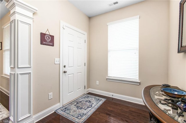 foyer featuring ornate columns, a healthy amount of sunlight, visible vents, dark wood finished floors, and baseboards