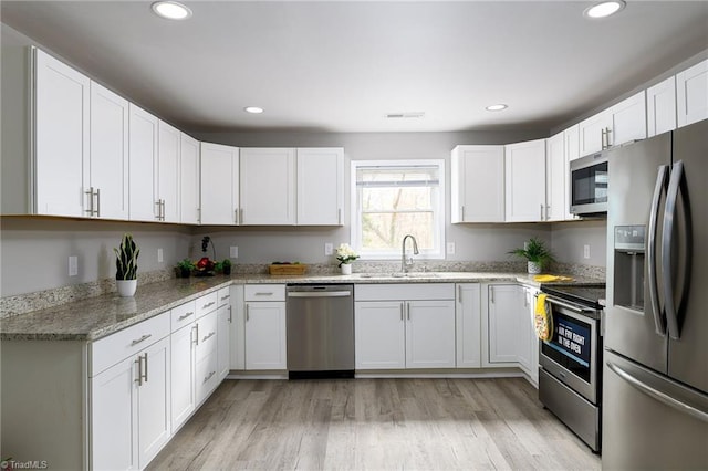 kitchen with sink, stainless steel appliances, white cabinets, and light stone countertops