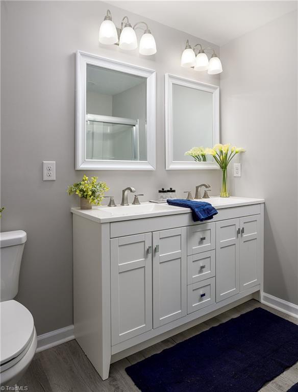 bathroom with hardwood / wood-style flooring, vanity, a shower with door, and toilet