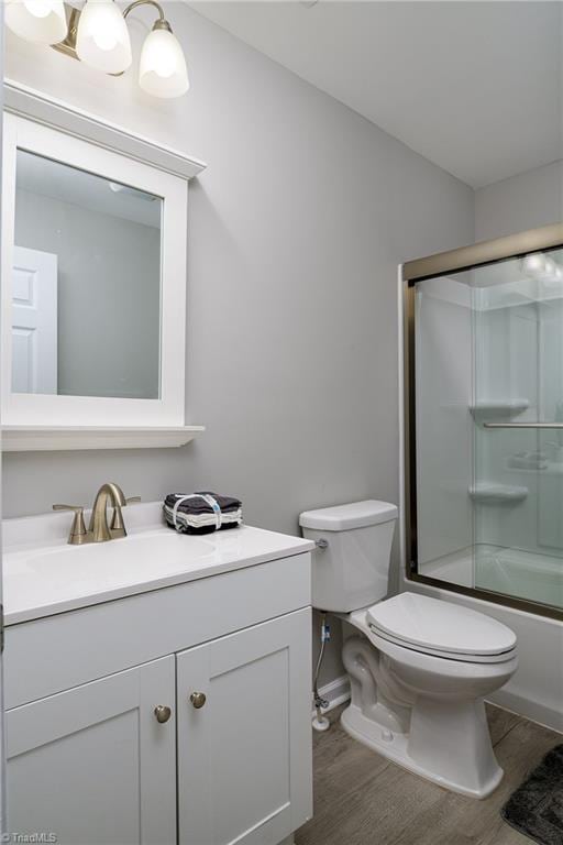 full bathroom featuring toilet, wood-type flooring, bath / shower combo with glass door, and vanity