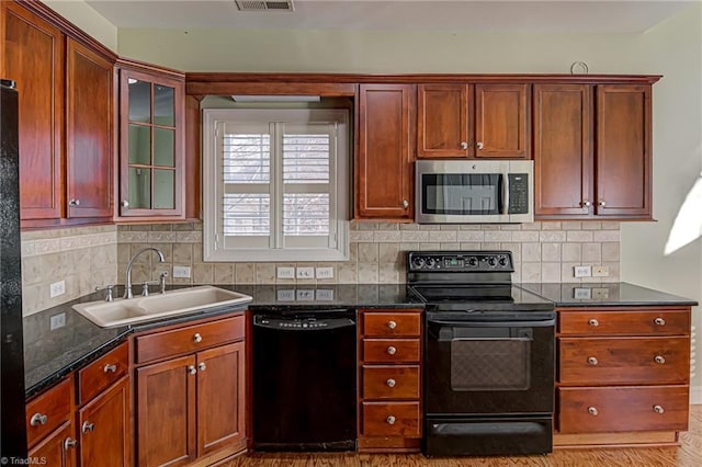 kitchen featuring sink, dark stone counters, decorative backsplash, black appliances, and light wood-type flooring