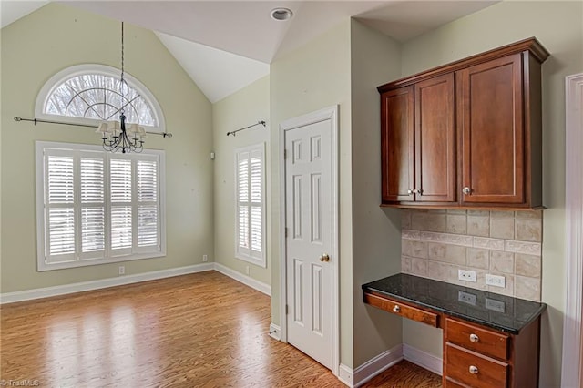 kitchen with backsplash, dark stone counters, vaulted ceiling, a notable chandelier, and wood-type flooring