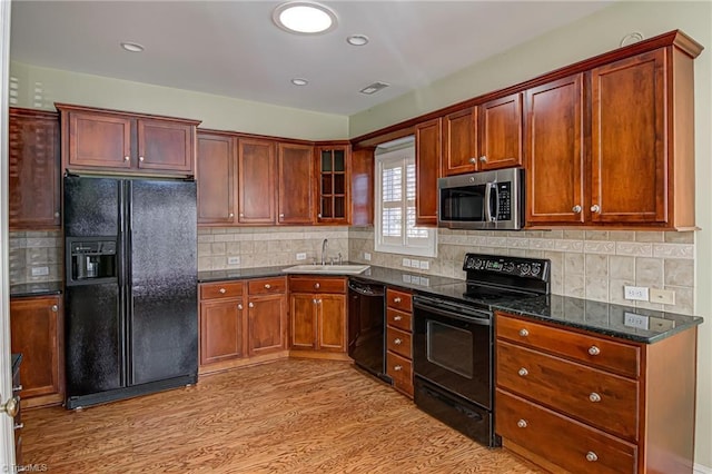 kitchen with sink, tasteful backsplash, dark stone countertops, black appliances, and light wood-type flooring