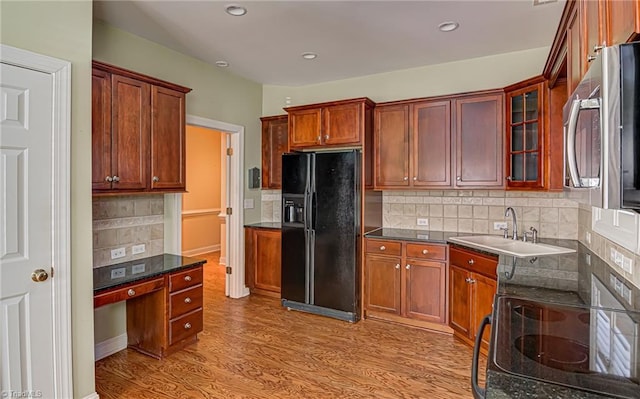 kitchen with stove, tasteful backsplash, black fridge, sink, and light hardwood / wood-style flooring