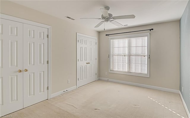 unfurnished bedroom featuring light carpet, ceiling fan, and two closets