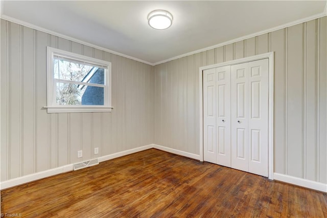 unfurnished bedroom with dark hardwood / wood-style flooring, crown molding, and a closet