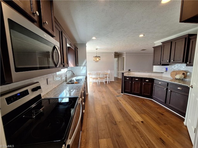 kitchen with dark brown cabinetry, a sink, appliances with stainless steel finishes, ornamental molding, and hardwood / wood-style floors