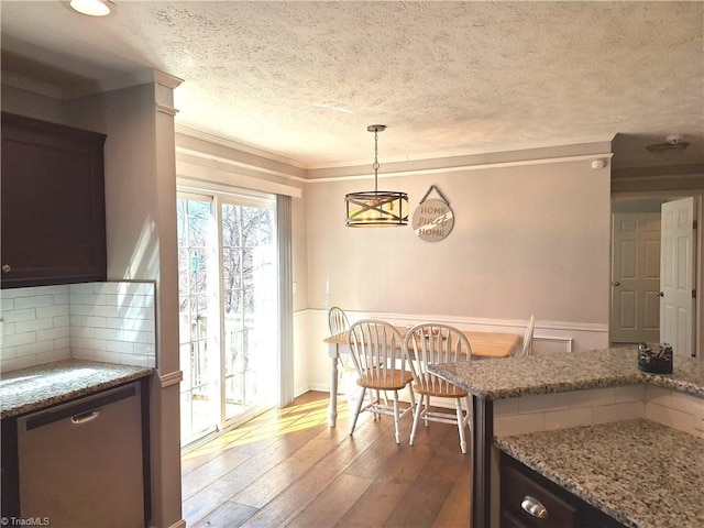 kitchen with light stone counters, hanging light fixtures, stainless steel dishwasher, decorative backsplash, and hardwood / wood-style floors