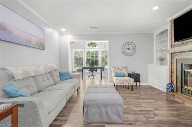 living room featuring a large fireplace, wood finished floors, crown molding, built in shelves, and recessed lighting