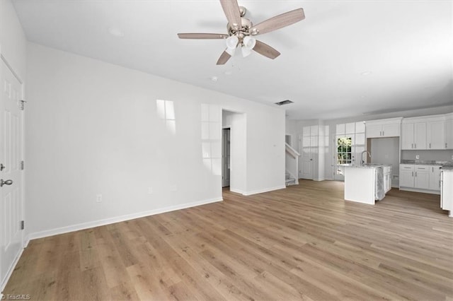 2154 E First St, Winston-Salem, NC 27101 - unfurnished living room with stairs, a ceiling fan, baseboards, and light wood-type flooring