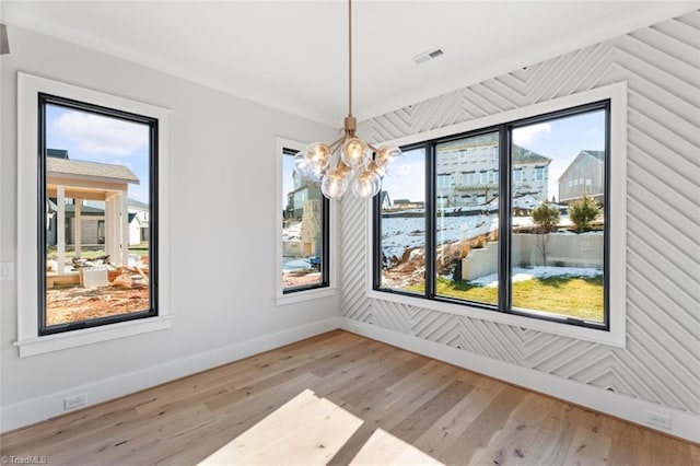 unfurnished dining area featuring visible vents, an inviting chandelier, baseboards, and wood finished floors