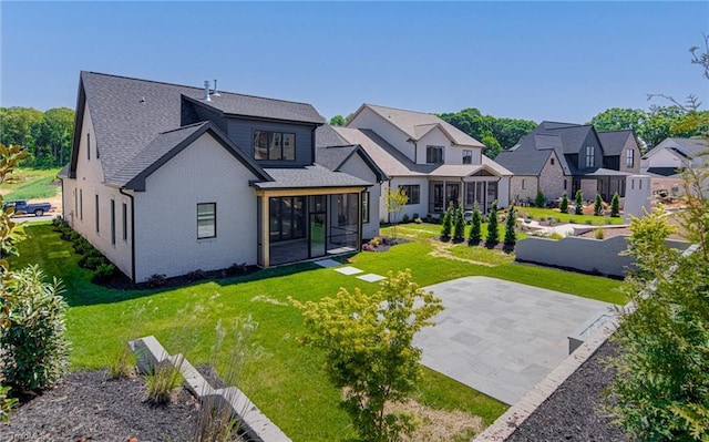 back of house with a sunroom, a patio area, a lawn, roof with shingles, and a residential view