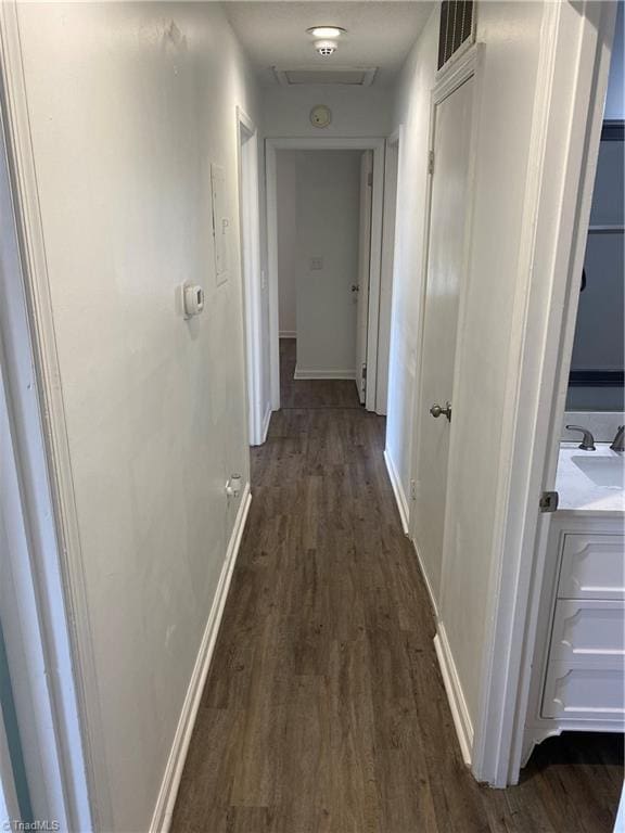 hall with a sink, baseboards, visible vents, and dark wood-type flooring