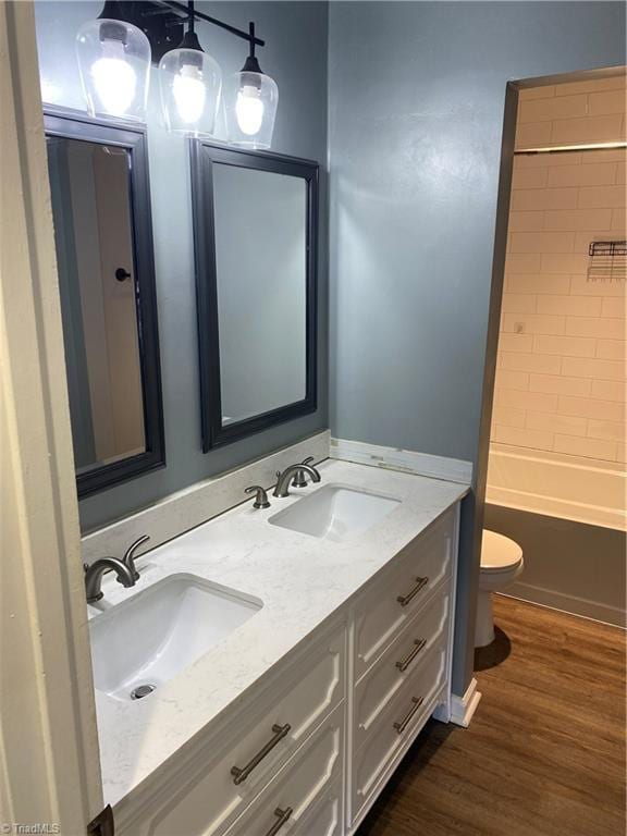 bathroom with toilet, double vanity, a sink, and wood finished floors