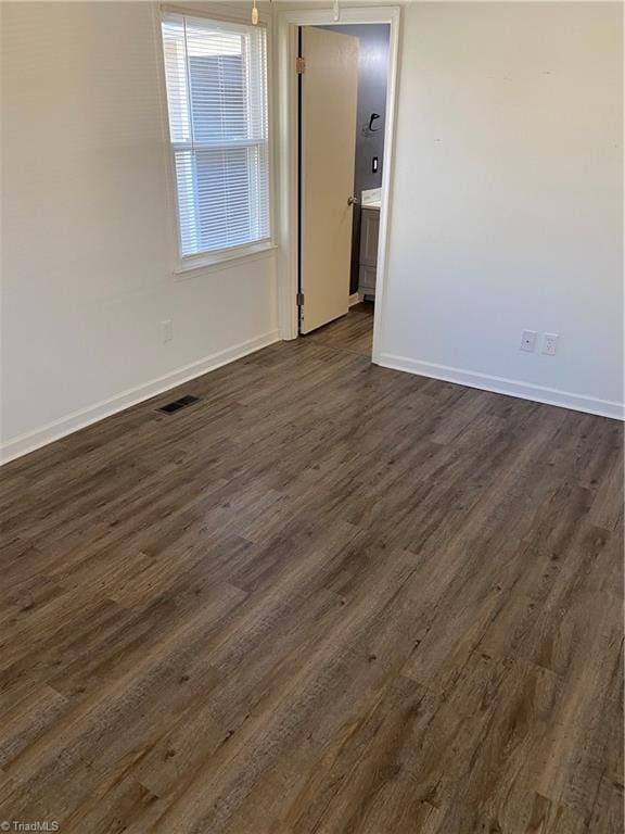 unfurnished room with visible vents, dark wood finished floors, and baseboards