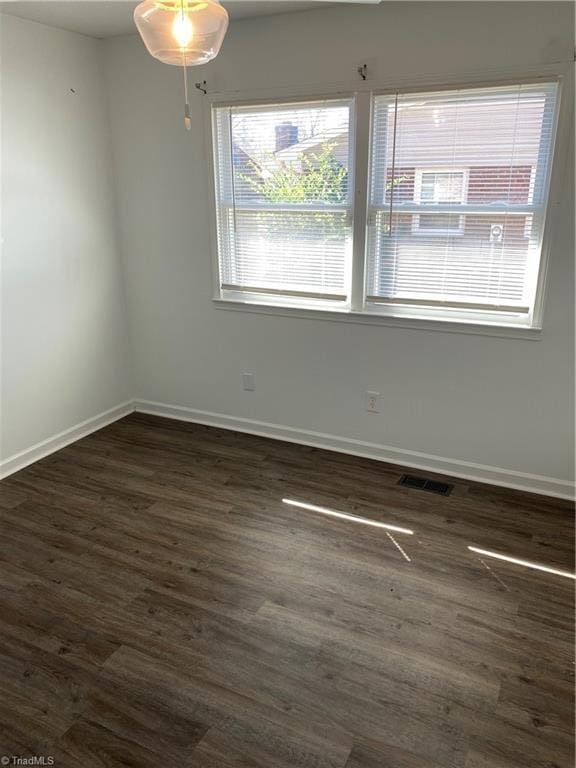 spare room with dark wood-style floors, visible vents, and baseboards