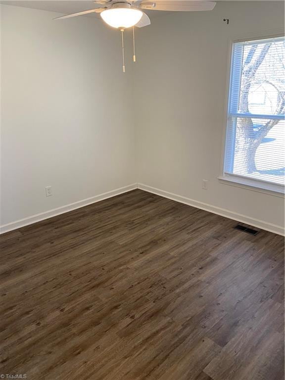 spare room with dark wood-style floors, visible vents, ceiling fan, and baseboards