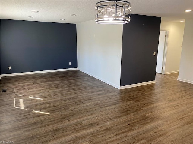 empty room featuring a notable chandelier, a textured ceiling, baseboards, and wood finished floors