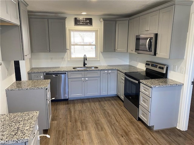 kitchen featuring light stone countertops, dark wood-type flooring, stainless steel appliances, and a sink