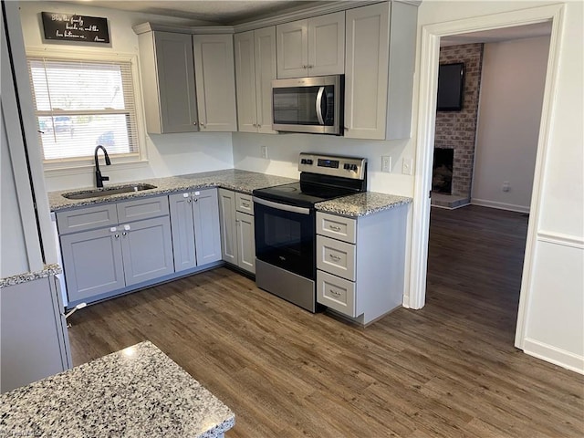 kitchen with light stone counters, gray cabinetry, appliances with stainless steel finishes, dark wood-type flooring, and a sink