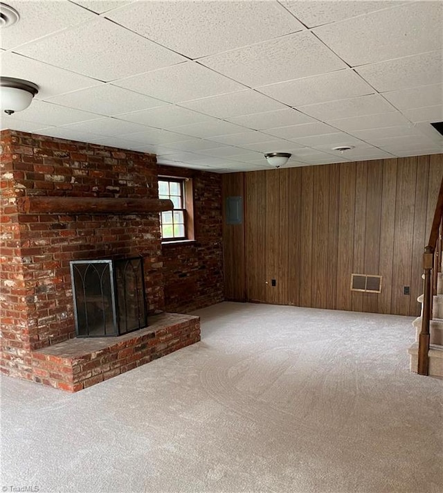 unfurnished living room featuring a brick fireplace, carpet floors, a paneled ceiling, and wood walls