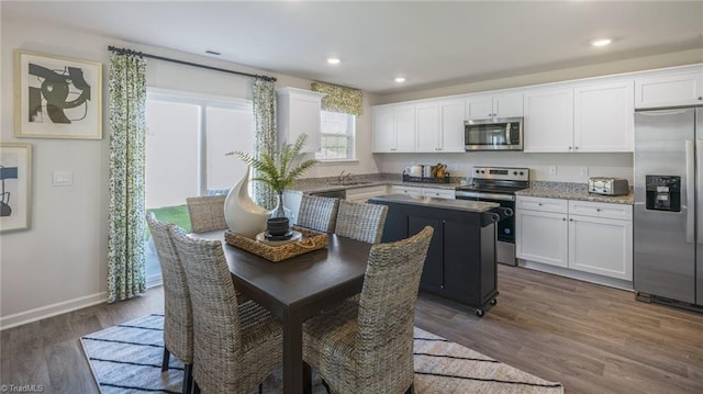 kitchen with appliances with stainless steel finishes, white cabinets, a center island, and dark hardwood / wood-style flooring