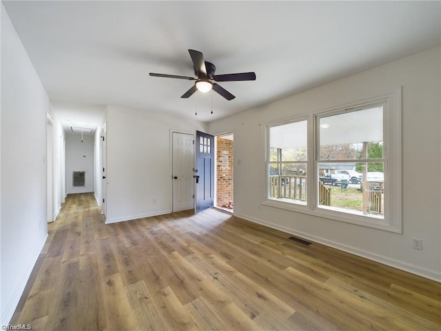 unfurnished living room with wood finished floors, baseboards, visible vents, attic access, and ceiling fan