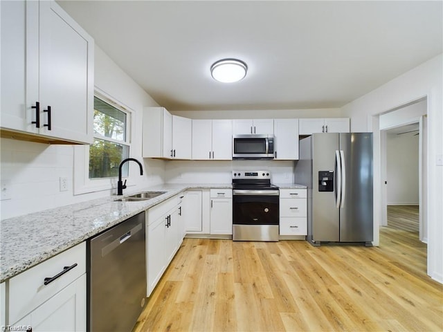 kitchen featuring light stone countertops, light wood-style flooring, a sink, stainless steel appliances, and white cabinetry